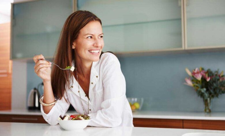 smiling happy woman eating food in kitchen 780x470 - چگونه کمتر غذا بخوریم؟ 15 راه مهار گرسنگی و کاهش اشتها